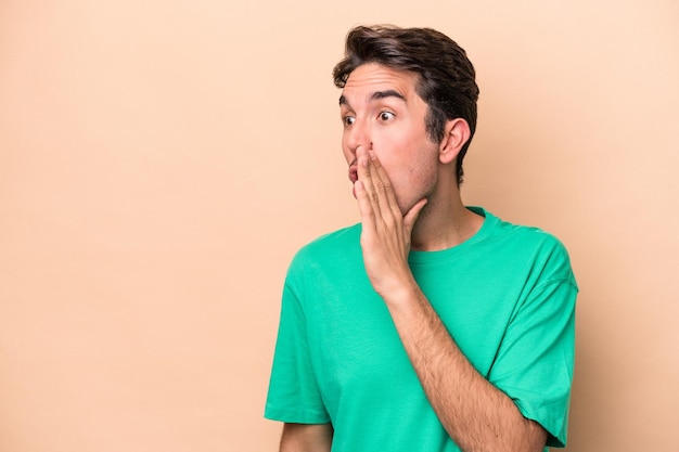 Jeune homme caucasien isolé sur fond beige étant choqué à cause de quelque chose qu'elle a vu.