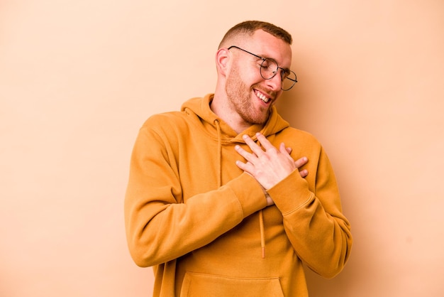 Jeune homme caucasien isolé sur fond beige a une expression amicale en appuyant sur la paume contre la poitrine Concept d'amour