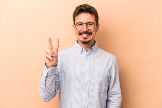 Jeune homme caucasien isolé sur fond beige joyeux et insouciant montrant un symbole de paix avec les doigts.