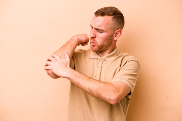 Jeune homme caucasien isolé sur fond beige massant le coude souffrant après un mauvais mouvement