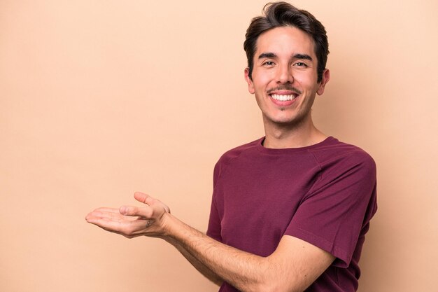 Jeune homme caucasien isolé sur fond beige tenant un espace de copie sur une paume