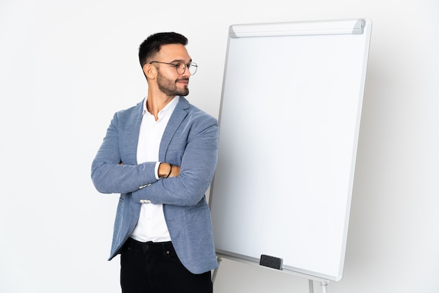 Jeune homme caucasien isolé sur fond blanc donnant une présentation sur tableau blanc et faisant le geste de doutes