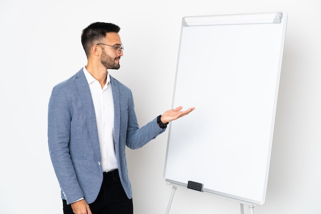 Jeune homme caucasien isolé sur fond blanc donnant une présentation sur tableau blanc