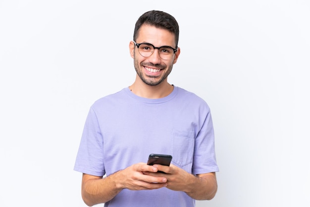 Jeune homme caucasien isolé sur fond blanc envoyant un message avec le mobile