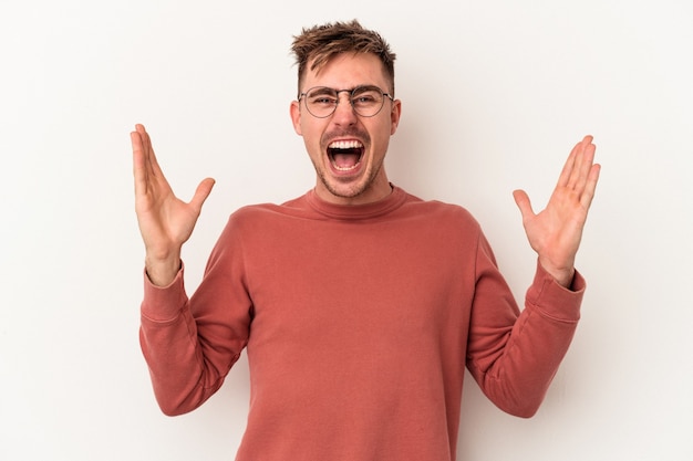 Jeune homme caucasien isolé sur fond blanc recevant une agréable surprise, excité et levant les mains.