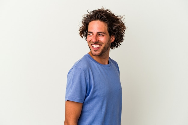 Jeune homme caucasien isolé sur fond blanc regarde de côté souriant, joyeux et agréable.