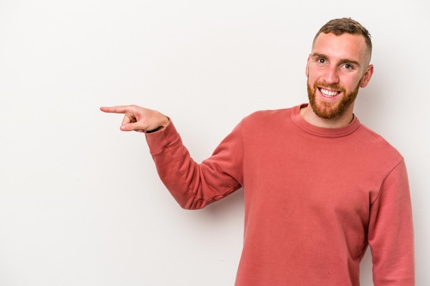 Jeune homme caucasien isolé sur fond blanc souriant joyeusement pointant avec l'index loin.