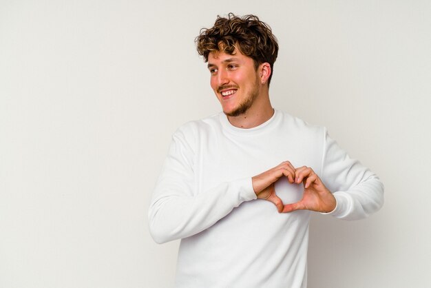 Jeune homme caucasien isolé sur fond blanc souriant et montrant une forme de coeur avec les mains.