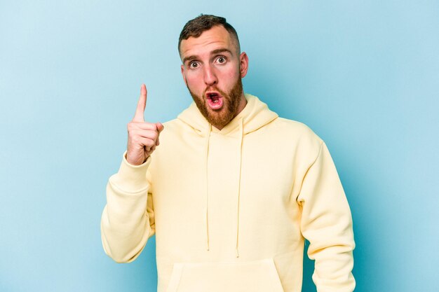 Jeune homme caucasien isolé sur fond bleu ayant une excellente idée de concept de créativité