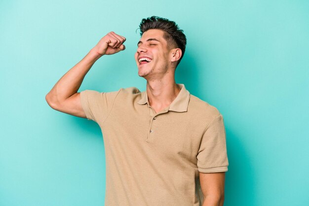 Jeune homme caucasien isolé sur fond bleu célébrant une victoire passion et enthousiasme expression heureuse