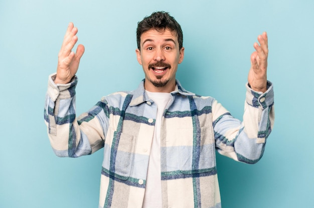 Jeune homme caucasien isolé sur fond bleu célébrant une victoire ou un succès, il est surpris et choqué.