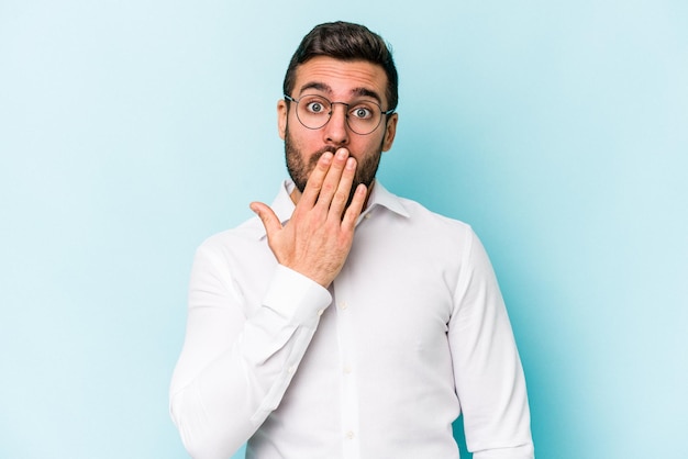 Jeune homme caucasien isolé sur fond bleu choqué couvrant la bouche avec les mains soucieux de découvrir quelque chose de nouveau