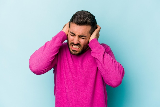 Jeune homme caucasien isolé sur fond bleu couvrant les oreilles avec les mains