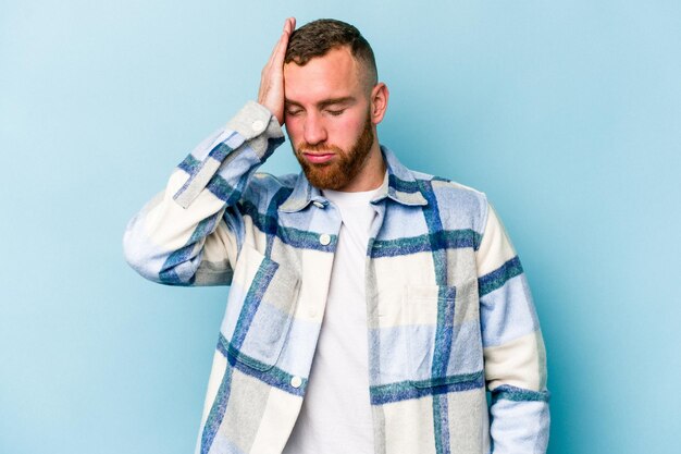 Jeune homme caucasien isolé sur fond bleu fatigué et très endormi en gardant la main sur la tête.