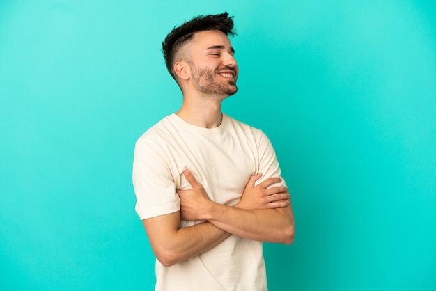 Jeune homme caucasien isolé sur fond bleu heureux et souriant