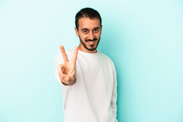 Jeune homme caucasien isolé sur fond bleu joyeux et insouciant montrant un symbole de paix avec les doigts.