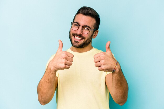 Jeune homme caucasien isolé sur fond bleu levant les deux pouces vers le haut souriant et confiant