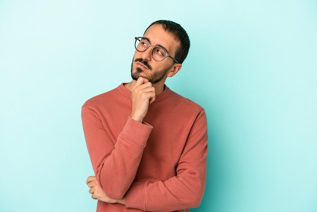 Jeune homme caucasien isolé sur fond bleu pensant et levant les yeux réfléchissant en contemplant avoir un fantasme