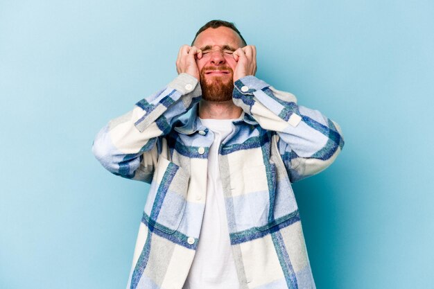 Jeune homme caucasien isolé sur fond bleu pleurant, mécontent de quelque chose, concept d'agonie et de confusion.