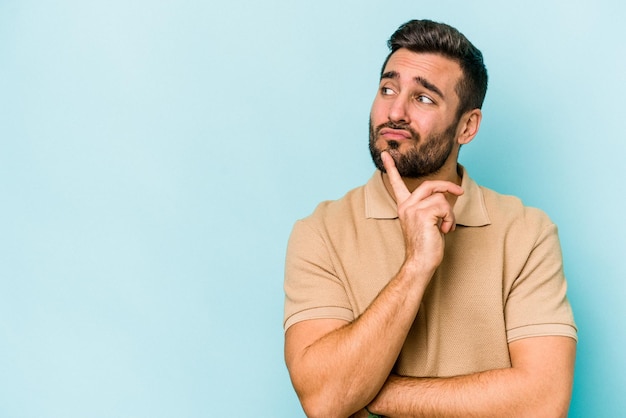 Jeune homme caucasien isolé sur fond bleu regardant de côté avec une expression douteuse et sceptique