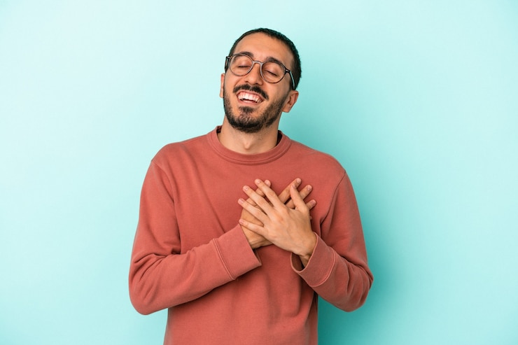 Photo jeune homme caucasien isolé sur fond bleu en riant en gardant les mains sur le cœur, concept de bonheur.