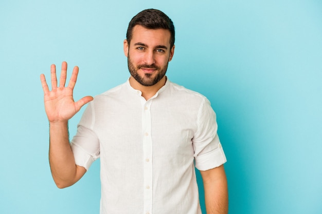 Jeune homme caucasien isolé sur fond bleu souriant joyeux montrant le numéro cinq avec les doigts.