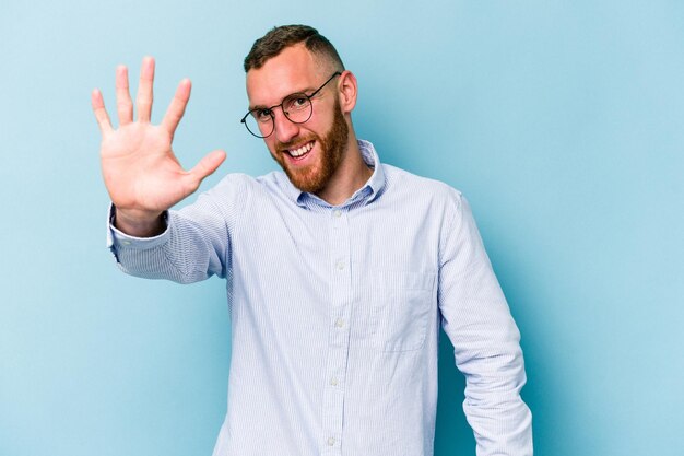 Jeune homme caucasien isolé sur fond bleu souriant joyeux montrant le numéro cinq avec les doigts