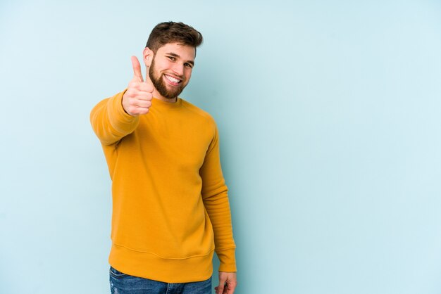 Jeune homme caucasien isolé sur fond bleu souriant et levant le pouce vers le haut