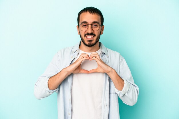 Jeune homme caucasien isolé sur fond bleu souriant et montrant une forme de coeur avec les mains.