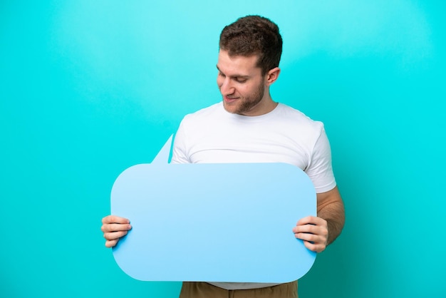 Jeune homme caucasien isolé sur fond bleu tenant une bulle vide