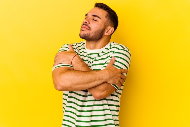 Jeune homme caucasien isolé sur fond jaune câlins, souriant insouciant et heureux.