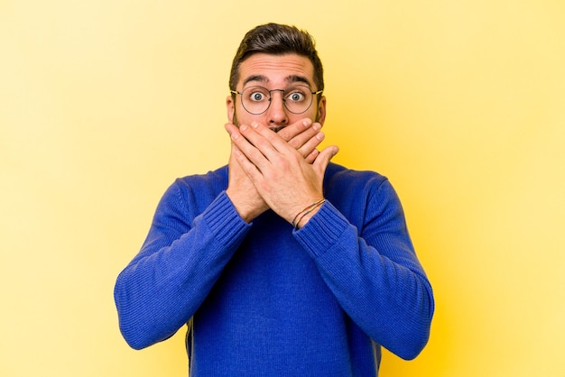 Jeune homme caucasien isolé sur fond jaune choqué couvrant la bouche avec les mains