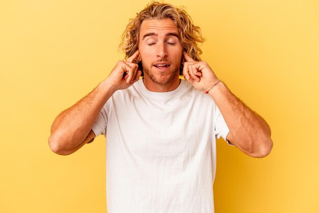 Jeune homme caucasien isolé sur fond jaune couvrant les oreilles avec les doigts, stressé et désespéré par une ambiance bruyante.