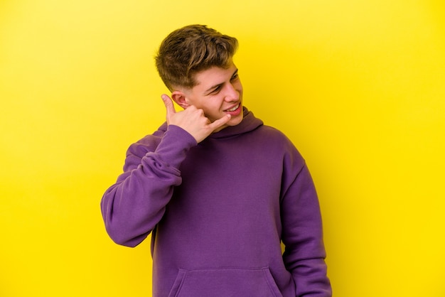 Jeune homme caucasien isolé sur fond jaune montrant un geste d'appel de téléphone mobile avec les doigts.
