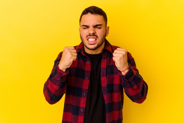 Jeune homme caucasien isolé sur fond jaune montrant le poing à la caméra, expression faciale agressive.