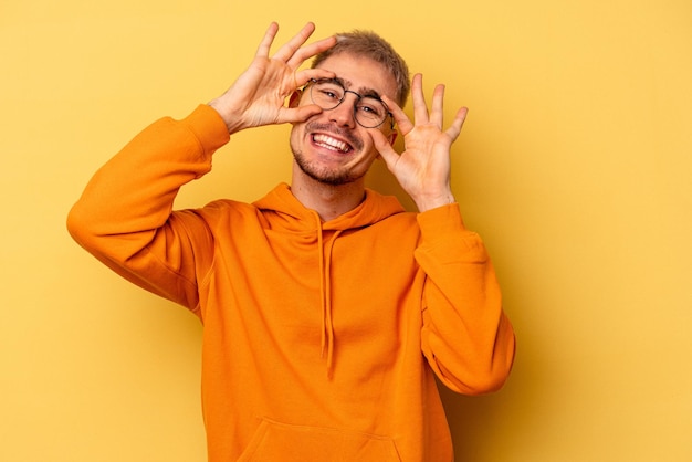 Jeune homme caucasien isolé sur fond jaune montrant un signe correct sur les yeux