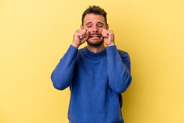 Jeune homme caucasien isolé sur fond jaune pleurnichant et pleurant tristement.