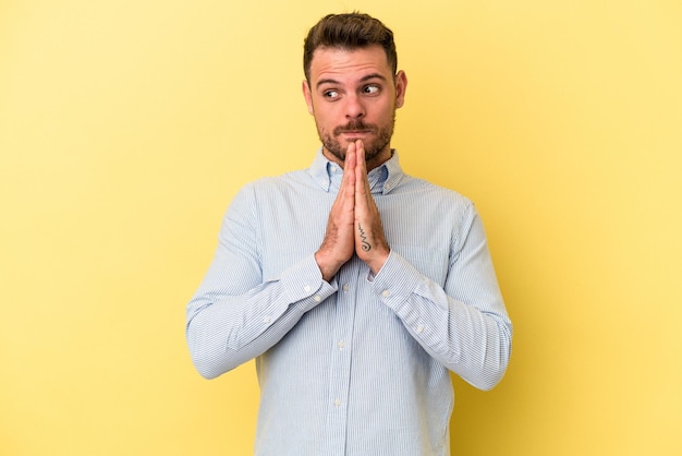 Jeune homme caucasien isolé sur fond jaune priant montrant la dévotion personne religieuse à la recherche d'inspiration divine