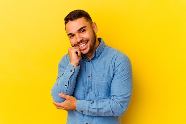 Jeune homme caucasien isolé sur fond jaune souriant heureux et confiant, touchant le menton avec la main.