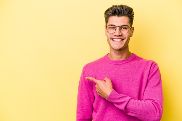 Jeune homme caucasien isolé sur fond jaune souriant et pointant de côté montrant quelque chose à l'espace vide