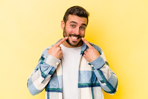 Jeune homme caucasien isolé sur fond jaune sourit pointant du doigt la bouche