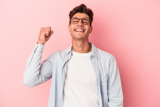 Jeune homme caucasien isolé sur fond rose célébrant une victoire, une passion et un enthousiasme, une expression heureuse.