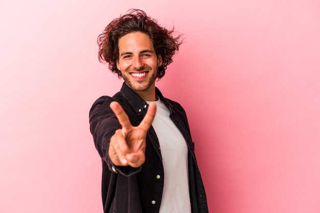 Jeune homme caucasien isolé sur fond rose joyeux et insouciant montrant un symbole de paix avec les doigts.