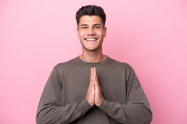 Jeune homme caucasien isolé sur fond rose maintient la paume ensemble La personne demande quelque chose