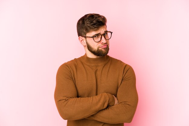 Jeune homme caucasien isolé sur fond rose malheureux à la recherche à huis clos avec une expression sarcastique.