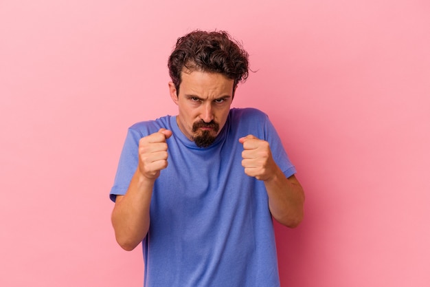 Jeune homme caucasien isolé sur fond rose montrant le poing à la caméra, expression faciale agressive.