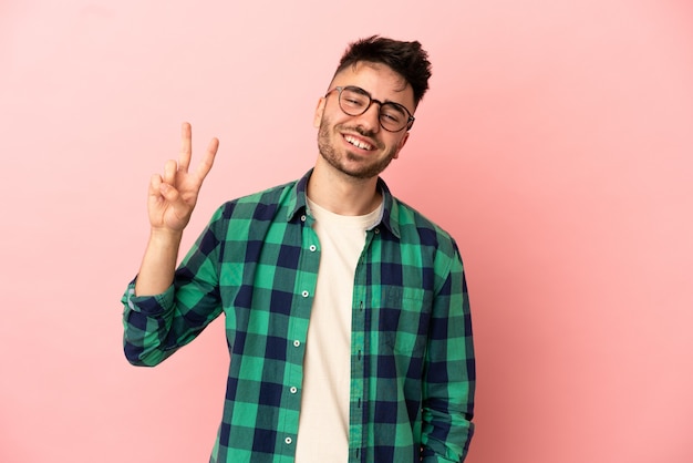 Jeune homme caucasien isolé sur fond rose souriant et montrant le signe de la victoire