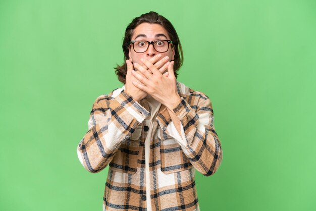 Jeune homme caucasien isolé sur fond vert chroma couvrant la bouche avec les mains