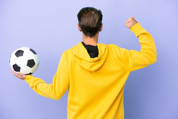 Jeune homme caucasien isolé sur fond violet avec ballon de foot