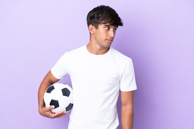 Jeune homme caucasien isolé sur fond violet avec ballon de foot